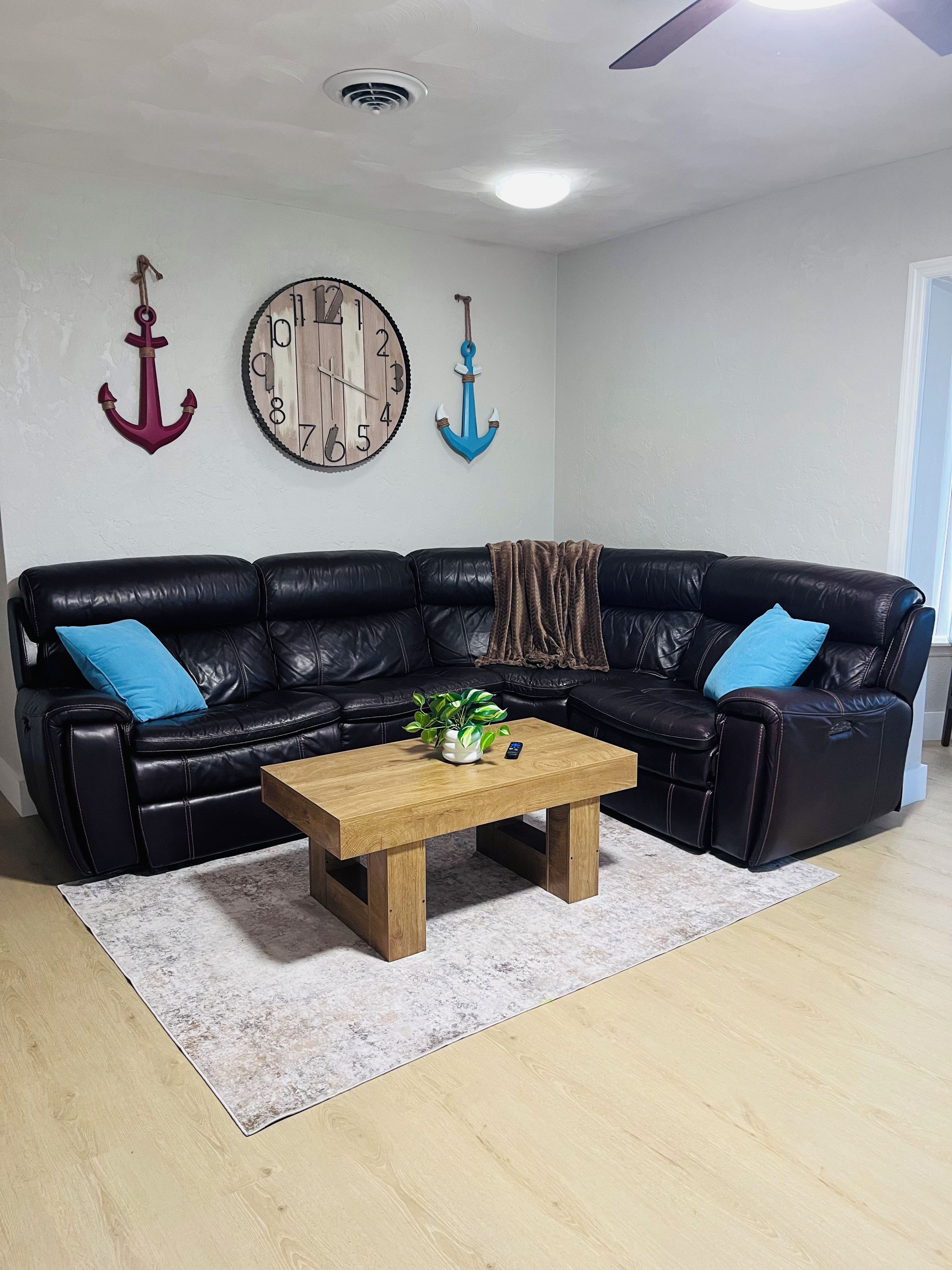 Ein Wohnzimmer mit einer schwarzen Ledersofa, einem Holztisch und einer Uhr an der Wand.