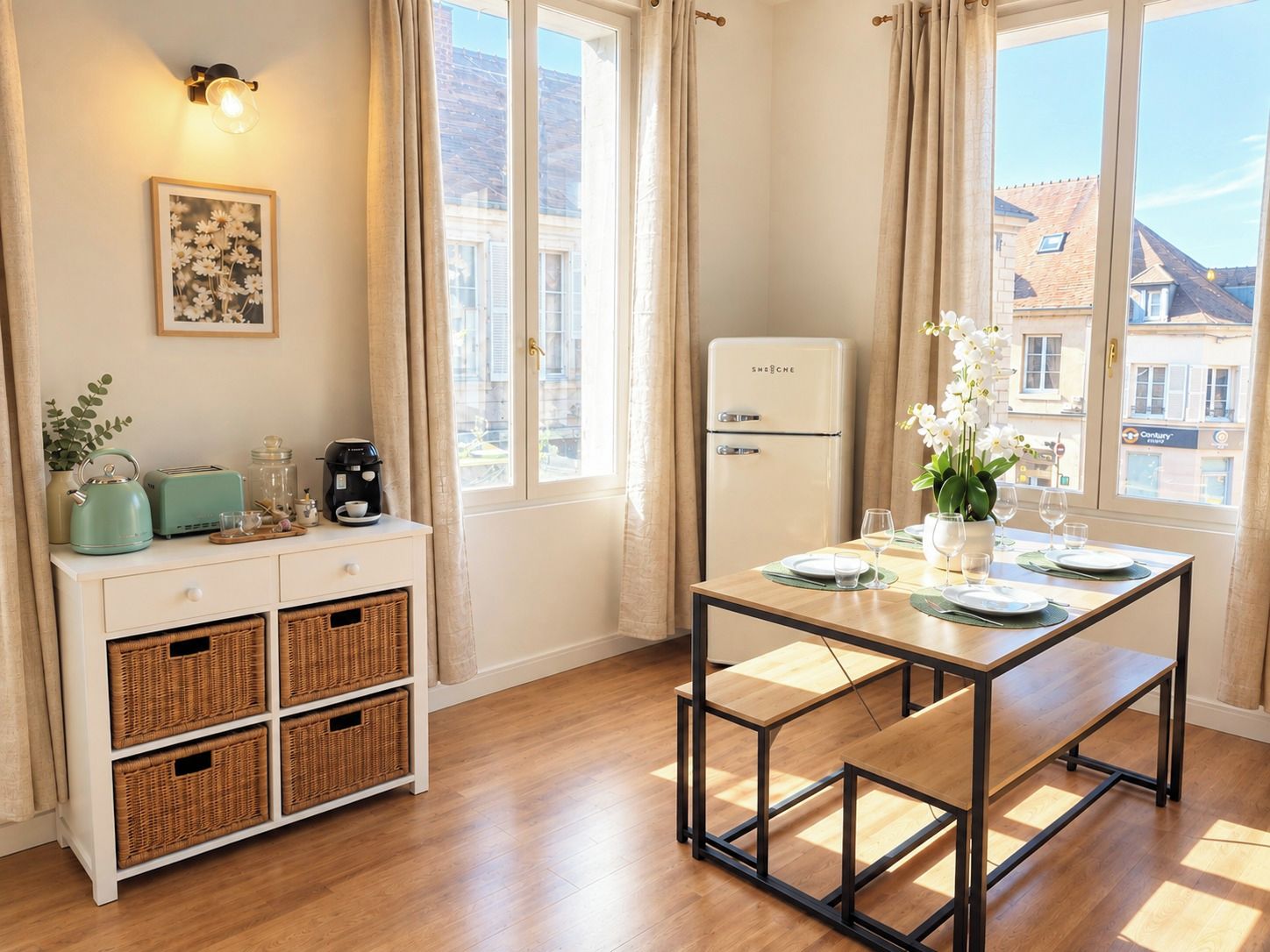 Una habitación con una mesa de comedor, un refrigerador blanco, un armario blanco con cestas y una lámpara fijada a la pared.
