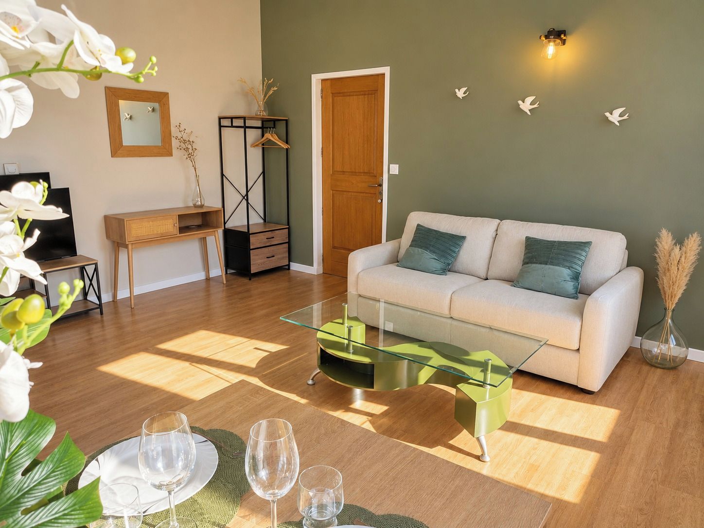 Ein Wohnzimmer mit einer Couch, einem Glastisch, einem Fernseher, einem Schreibtisch und einer Tür.