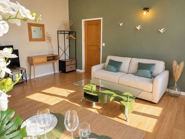 A living room with a sofa, a glass coffee table, a TV, a desk, and a door. - New Listing (Compiègne)
