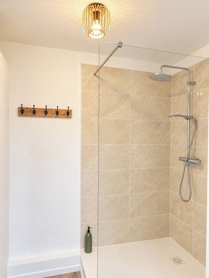 A modern bathroom with a glass shower enclosure, a wooden coat rack, and a single bottle of shampoo. - New Listing (Compiègne)