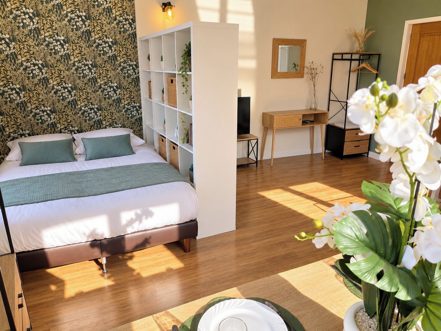Ein Schlafzimmer mit einem Bett, einem Schreibtisch, einem Kleiderschrank und einer Wand mit ornamentalem Wandpapier.