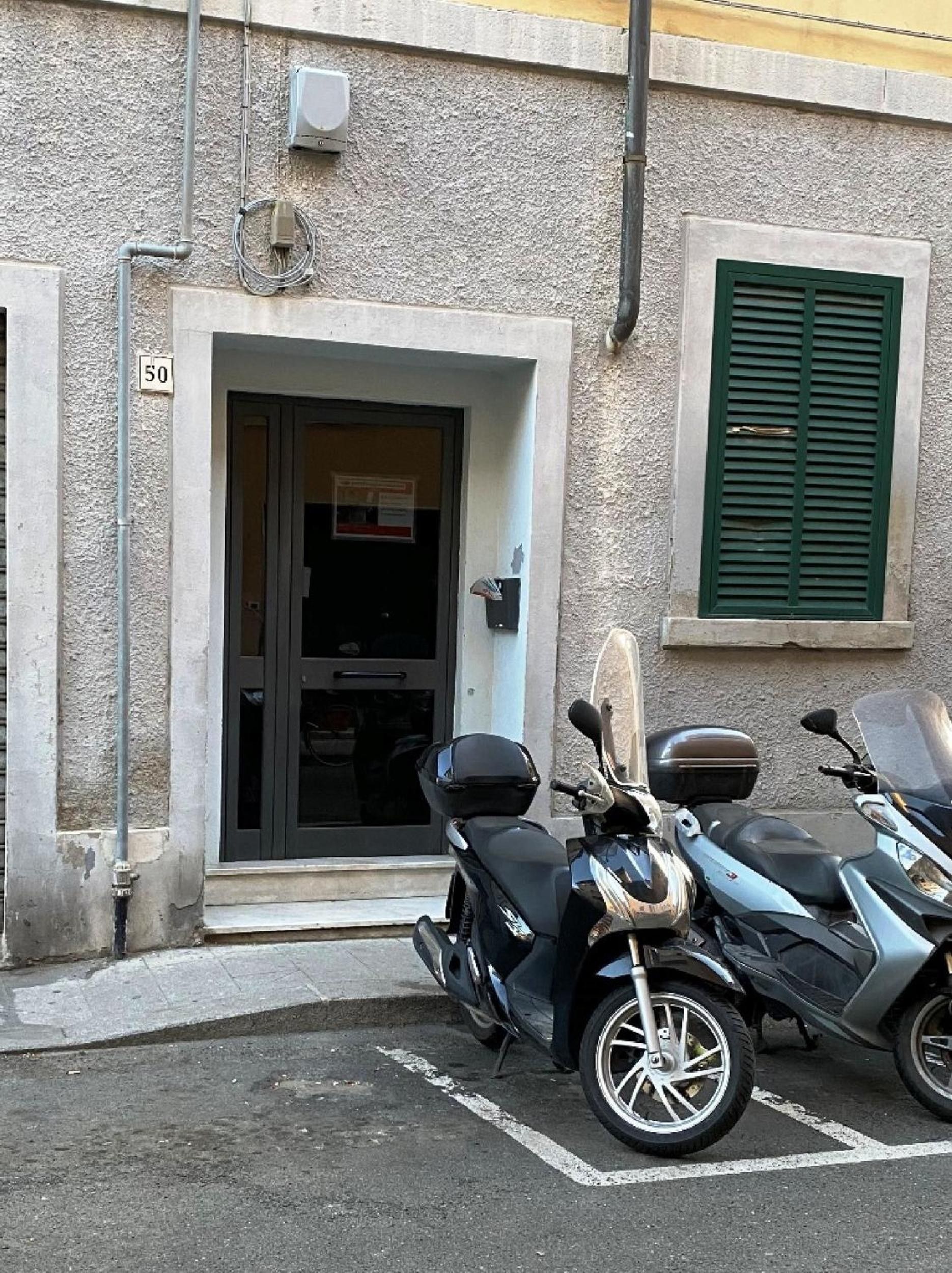 L’entrée d’un immeuble avec une porte, une fenêtre avec des volets et deux scooters garés.