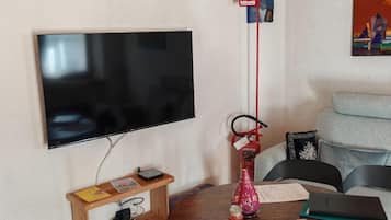 A living room with a flat-screen TV mounted on the wall, a wooden table with a vase, a fire extinguisher, and a sofa.