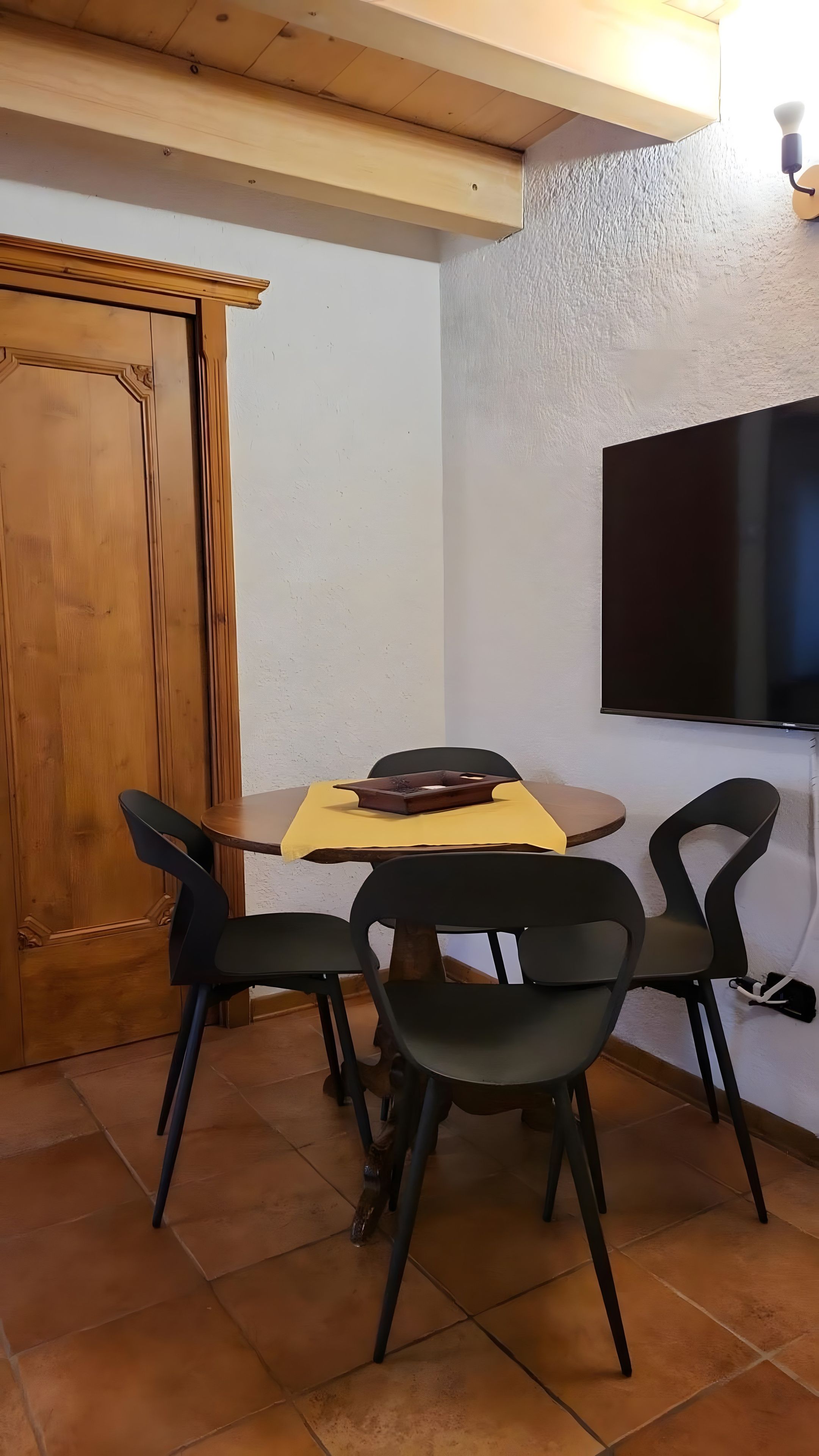 Ein Essbereich mit Holztisch, vier Stühlen, einem an der Wand befestigten Flachbildfernseher und einer Holztür.