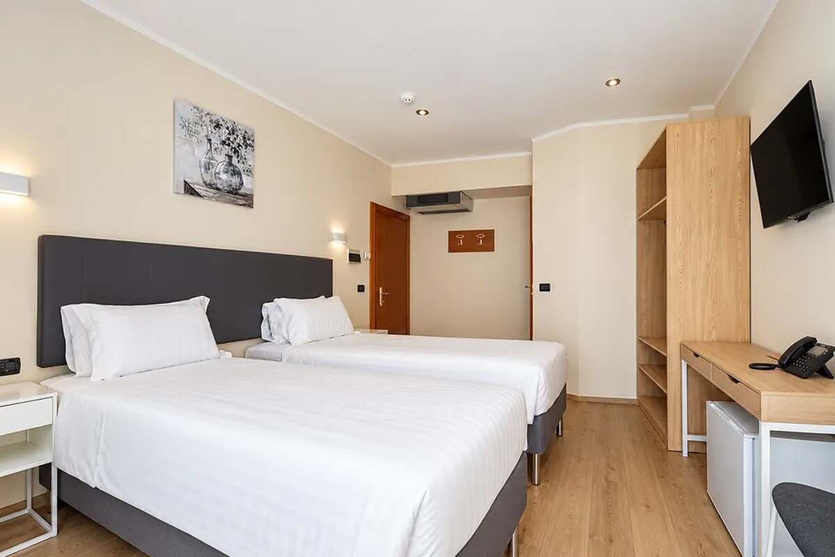 A hotel room with two beds, a desk, a television, and a painting on the wall.