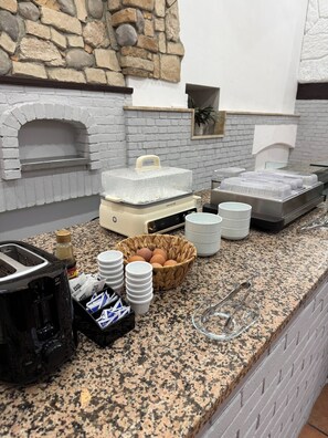 A kitchen area with a stone wall, a brick oven, a food warmer, and various kitchen utensils and appliances. - Hotel Innova Milano Nord (Cinisello Balsamo)