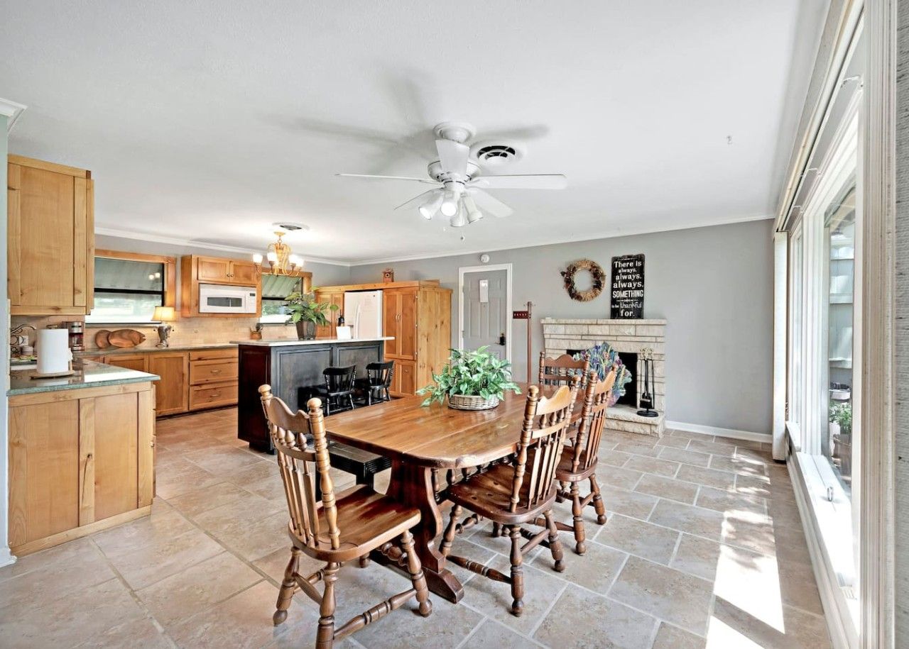 A spacious kitchen with wooden cabinets, a dining table with chairs, a ceiling fan, and a fireplace.
