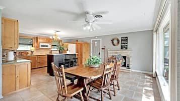 A spacious kitchen with wooden cabinets, a dining table with chairs, a ceiling fan, and a fireplace.