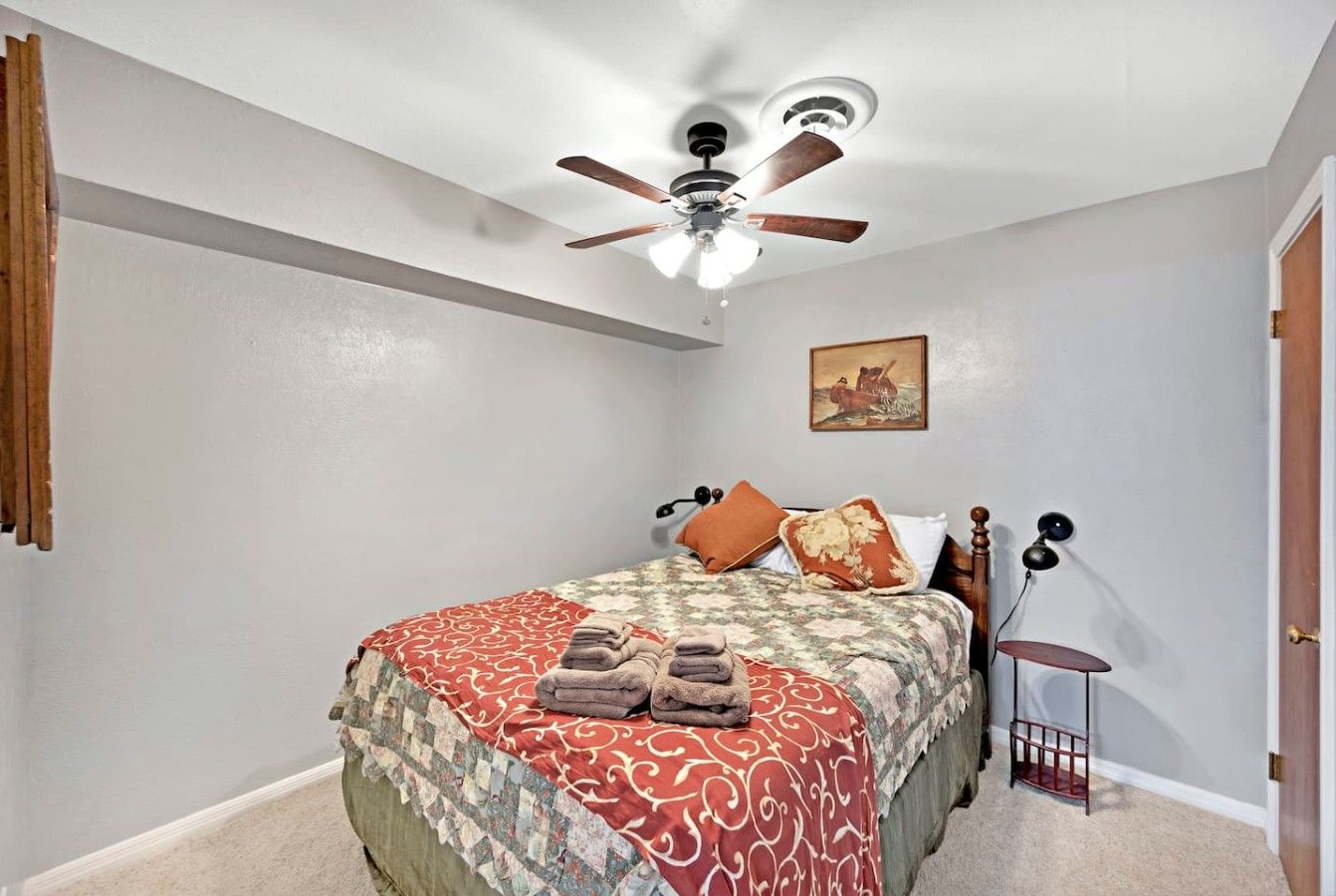 Un dormitorio con una cama, un ventilador de techo, una mesita de noche y una lámpara de pared.