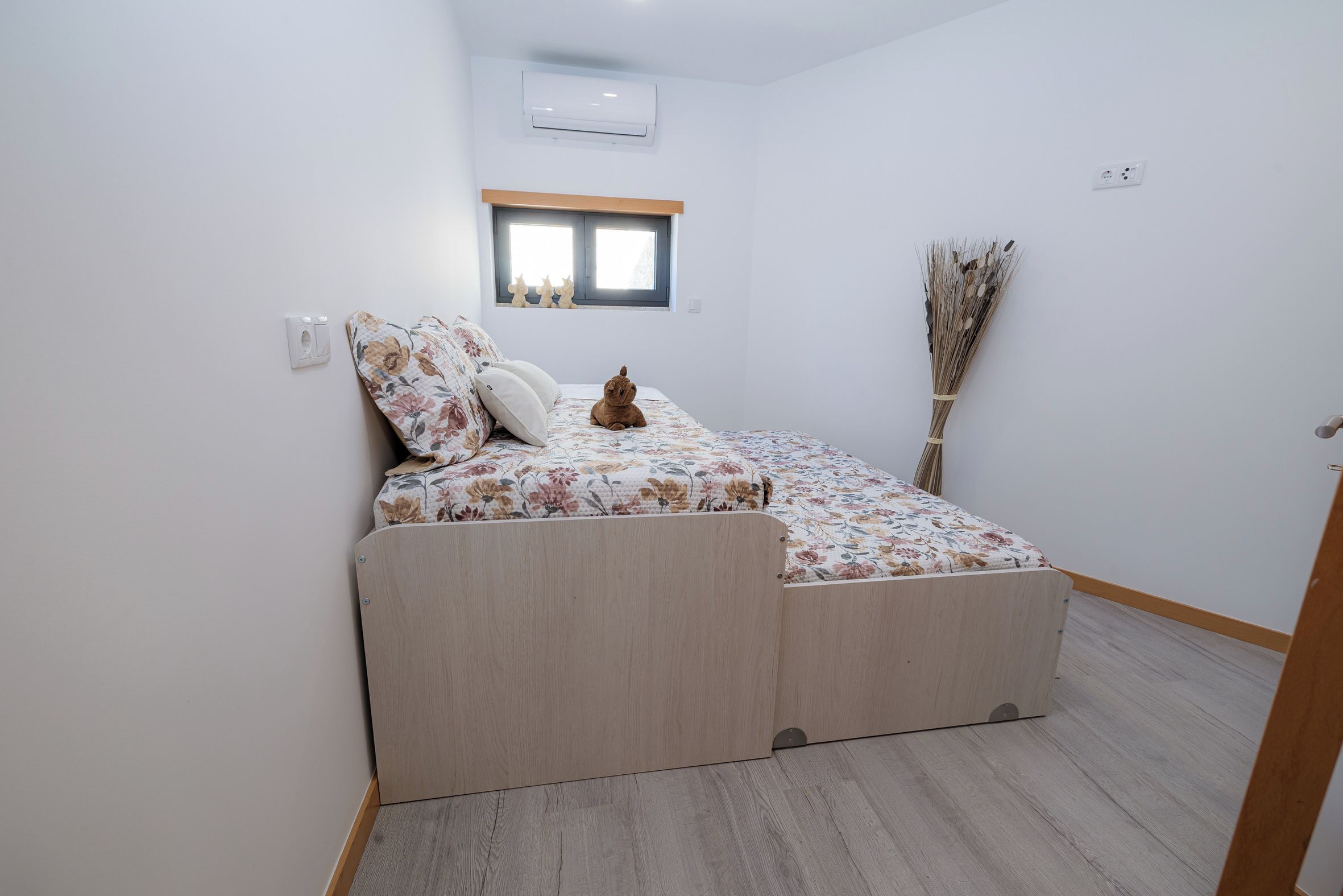 Una camera da letto piccola con un letto, una finestra, un condizionatore d'aria a parete e una scopa.