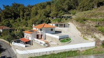 A modern two-story house with a red-tiled roof, a stone retaining wall, and a small garden area.