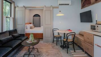 A compact hotel room with a sofa, a bed, a dining area with chairs, a small table, a microwave, and a TV on the wall.