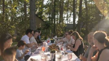 A group of people dining outdoors at a table with a white tablecloth, surrounded by trees.