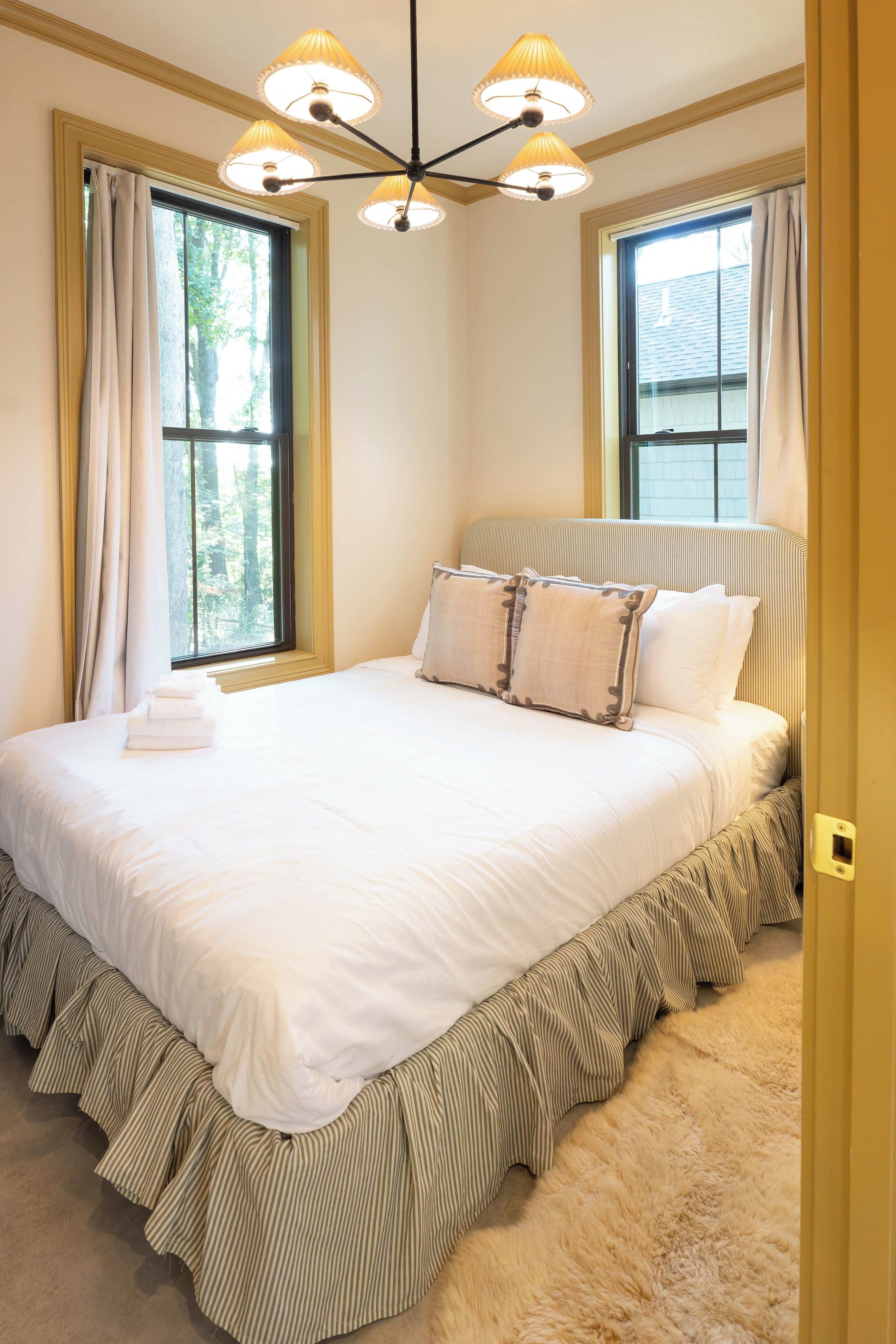 A bedroom with a large bed, a chandelier, and two windows with curtains.
