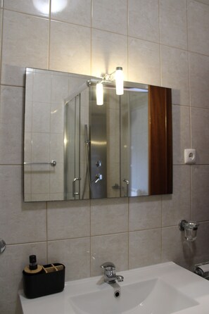 A bathroom with a large mirror, a sink, and a shower. - Douro Nest House -  (Resende)