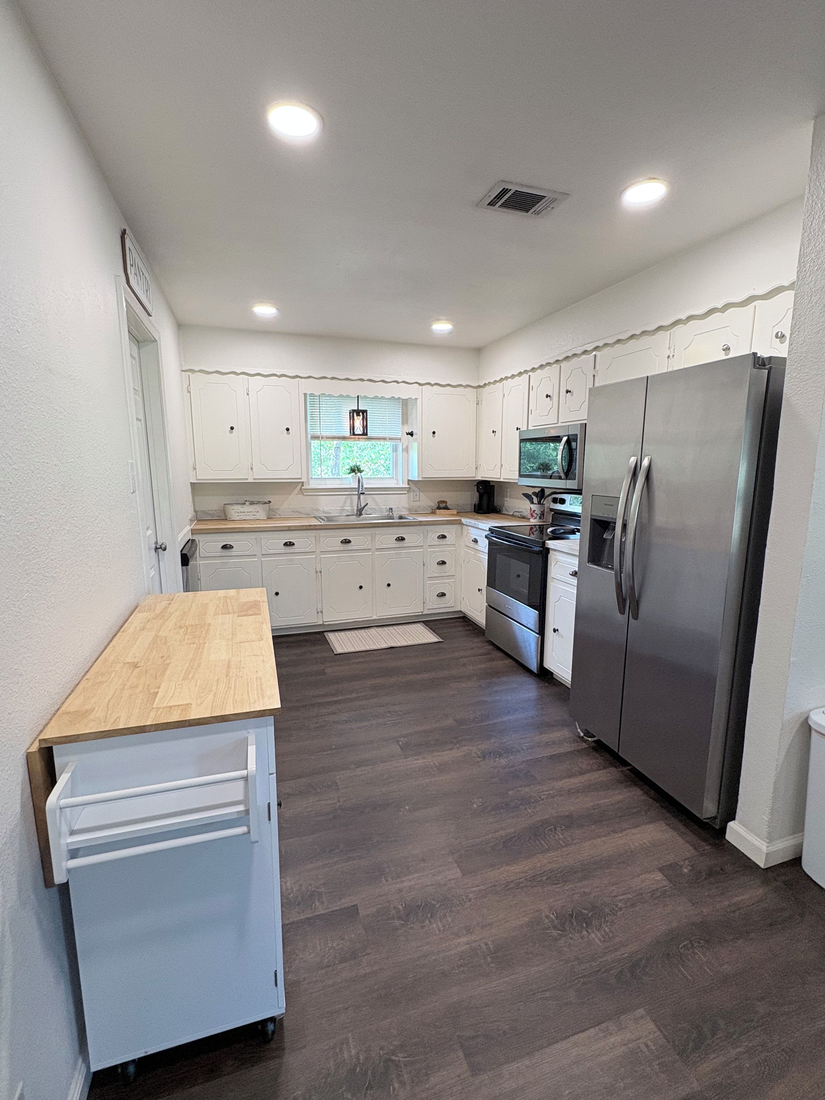 A modern kitchen with white cabinetry, a stainless steel refrigerator, and a wooden countertop.