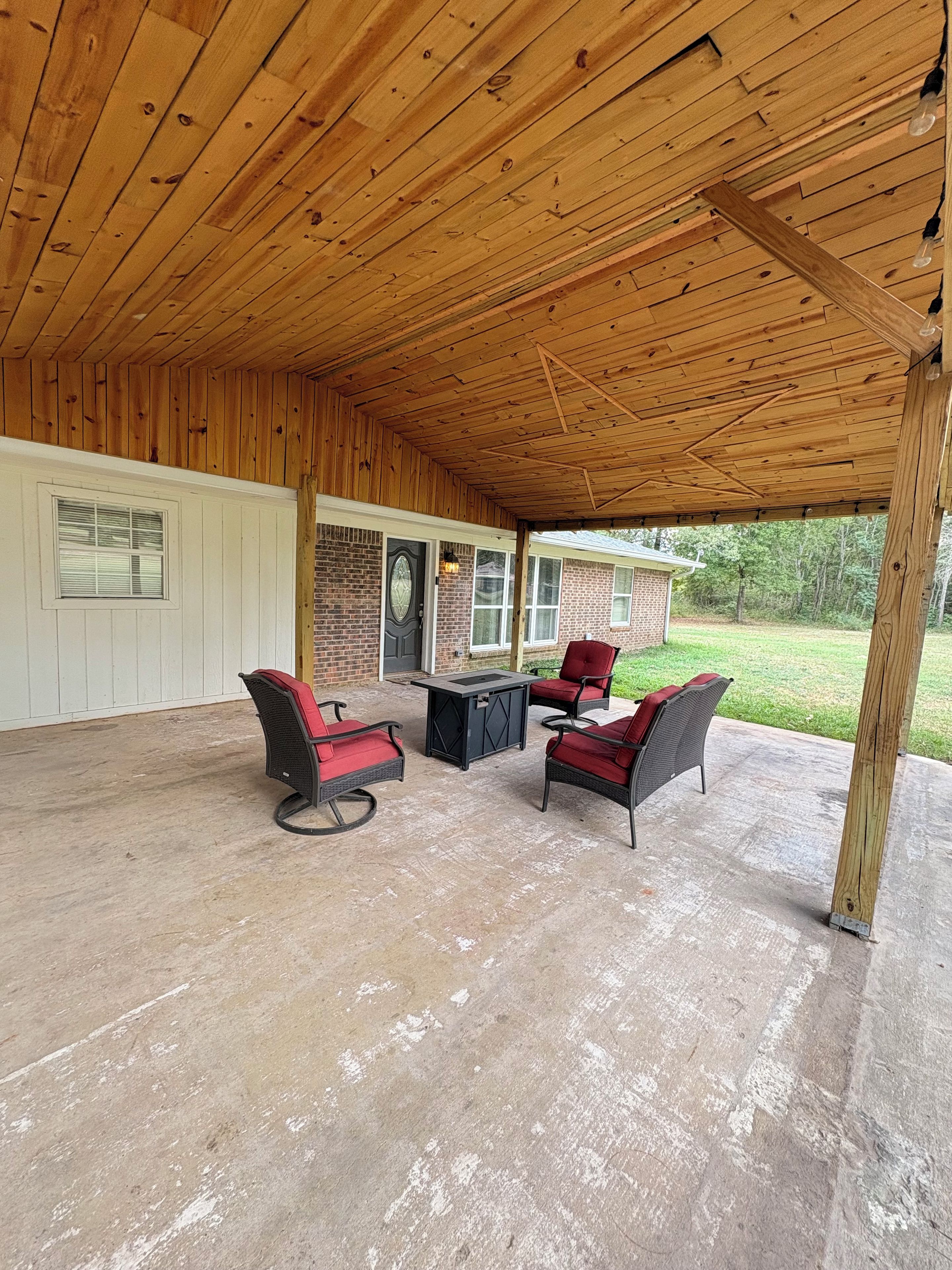 A covered patio area with outdoor furniture and a brick house in the background.
