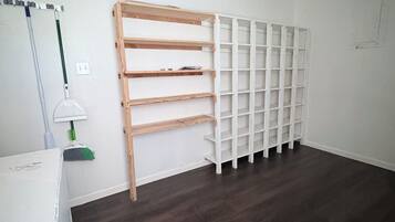 A room with a dark wooden floor, white walls, and a white shelving unit against the wall.