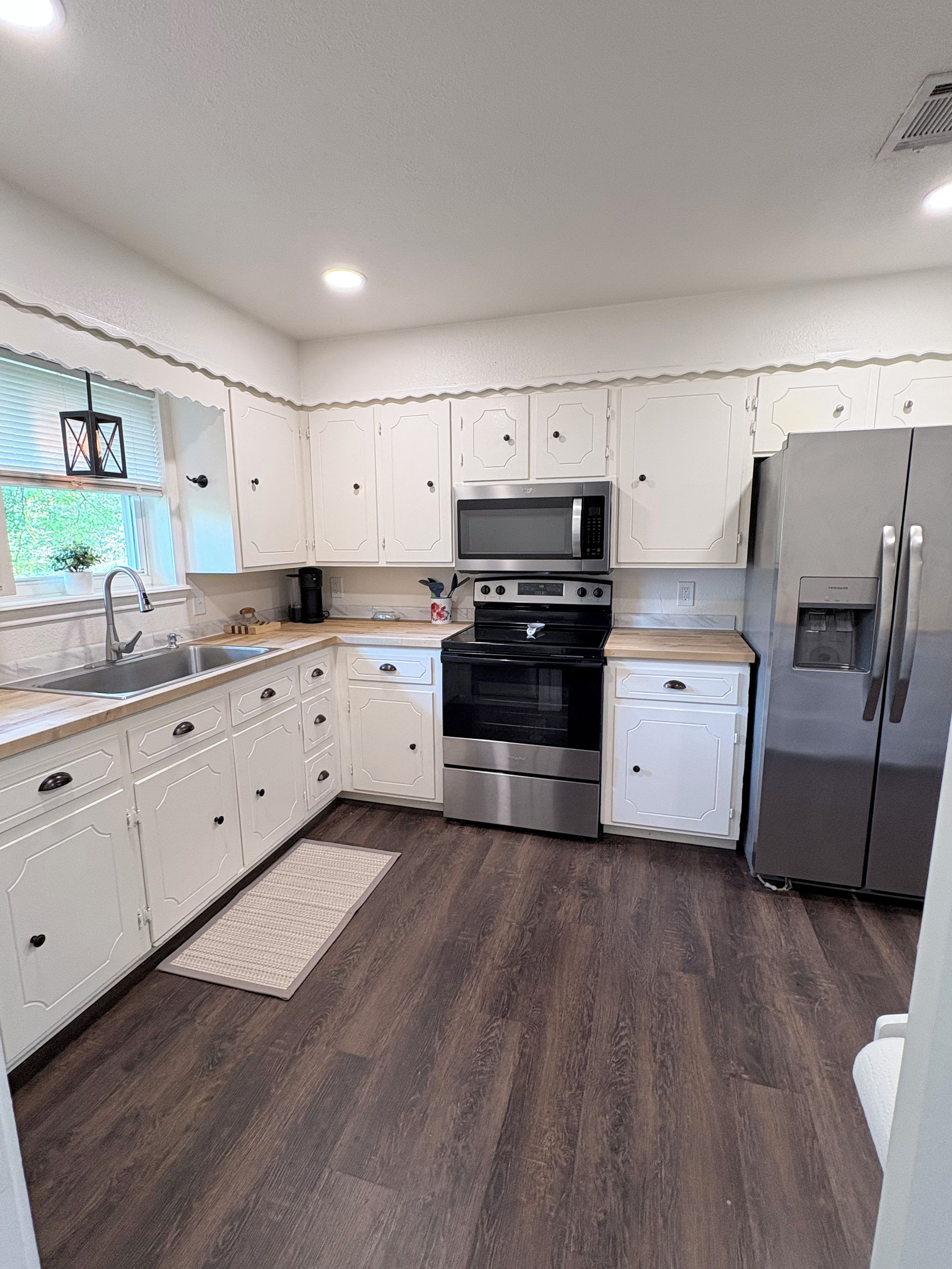 A modern kitchen with white cabinetry, stainless steel appliances, and a wooden floor.