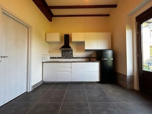 Cozinha com geladeira preta, armários brancos, painel de azulejos e vigas de madeira no teto.