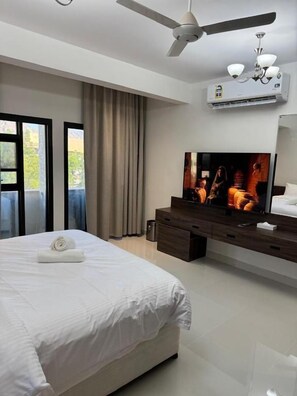 Una habitación de hotel moderna con una cama grande, un televisor de pantalla plana, un ventilador de techo y un equipo de aire acondicionado.
