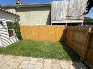 Un patio trasero con cerco de madera, un patio empedrado y un área con césped.