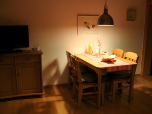 A dining area with a table, chairs, a television on a cabinet, and a clock on the wall.
