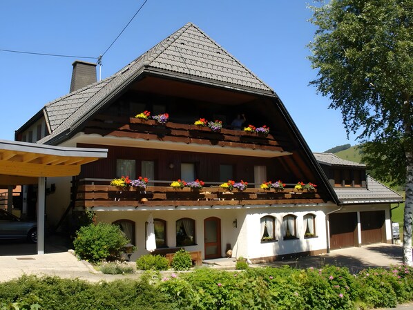 A two-story chalet with a sloped roof, wooden balconies with flower boxes, and a covered porch.