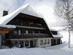 A snow-covered chalet with a sloped roof, wooden balconies, and multiple windows.