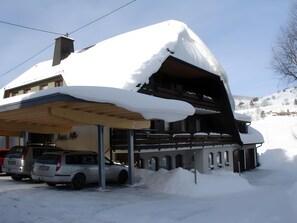 A building with a covered outdoor area, a car parked in front, and snow on the roof.