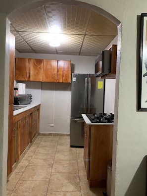 Una cocina compacta con muebles de madera, un refrigerador de acero inoxidable y un microondas.