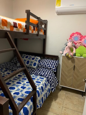 Una cama litera con ropa de cama estampada, un armario de madera y un aire acondicionado de pared.