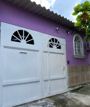 Una puerta de garaje blanca con un diseño de ventana circular, una puerta blanca con manija y un ventanal pequeño con barandillas decorativas.
