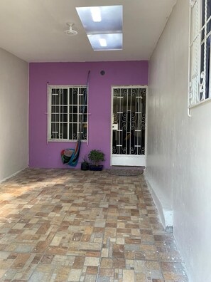 Una habitación con piso de baldosas, pared morada y una ventana con barrotes.