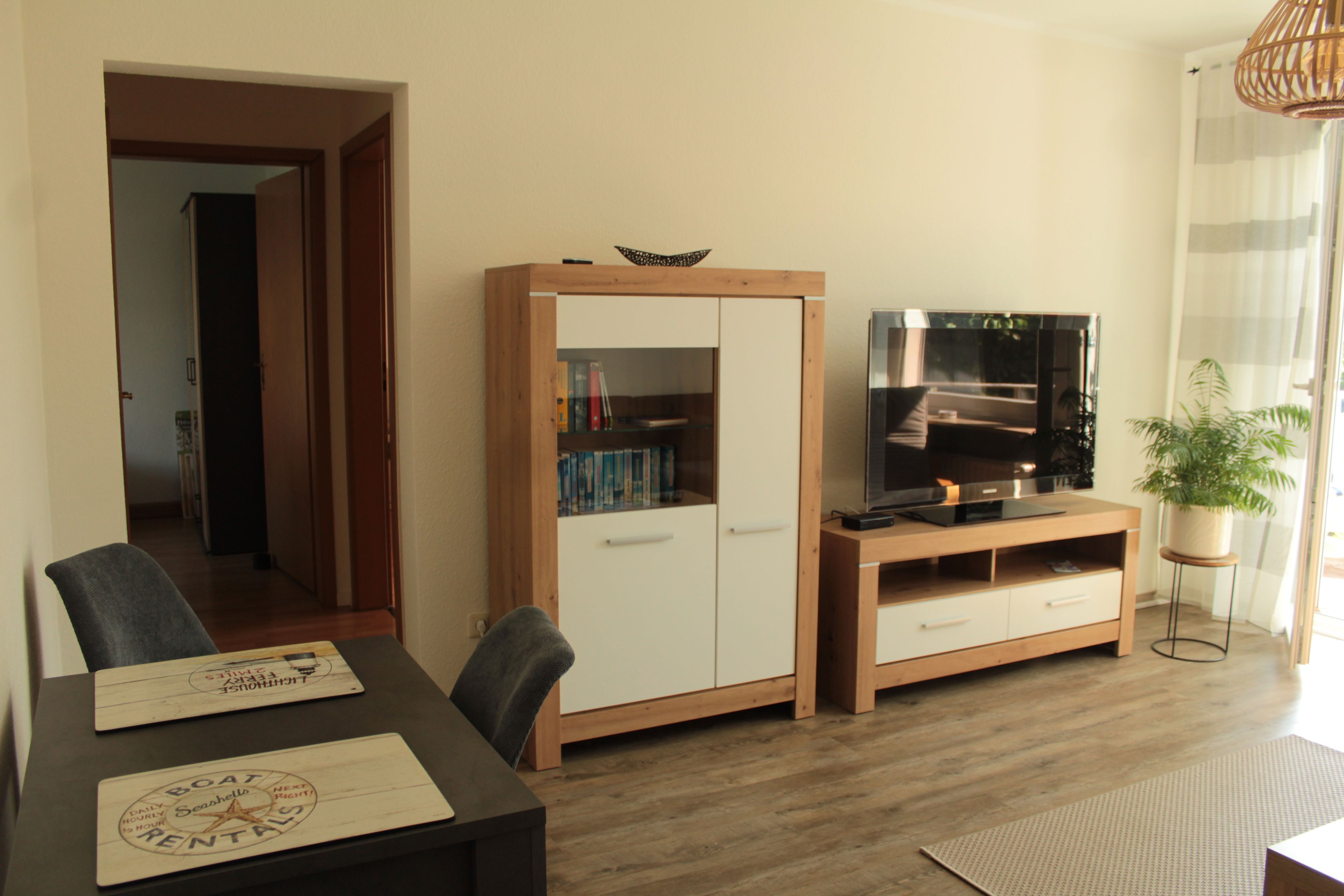 A living room with a wooden cabinet, a television on a stand, a dining table with chairs, and a potted plant.