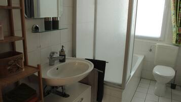 Ein Badezimmer mit weißem Waschbecken, einem Spiegel, einem Handtuchhalter, einer Toilette und einer Badewanne.