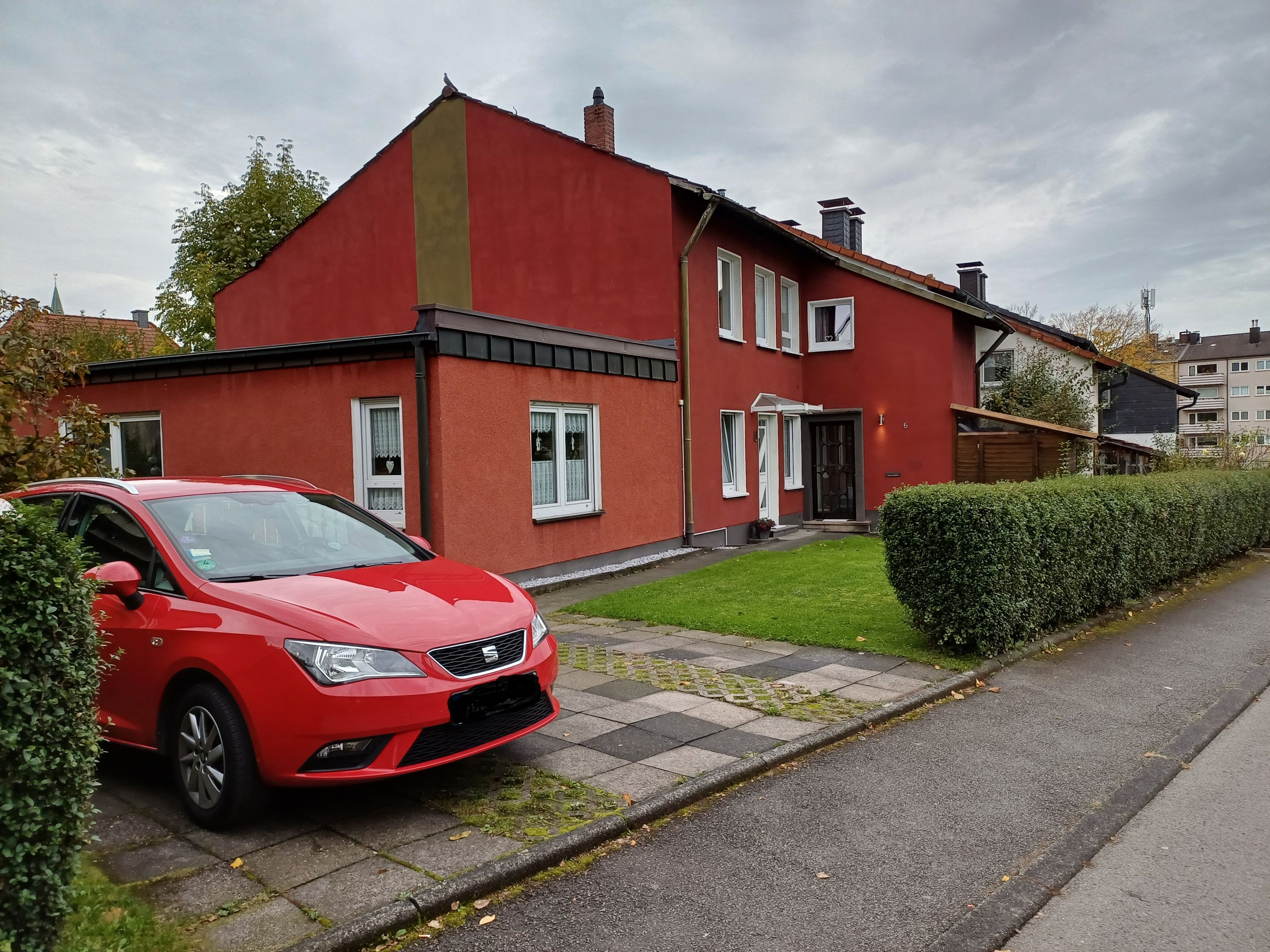 A red two-story house with a paved driveway and a red car parked in front.