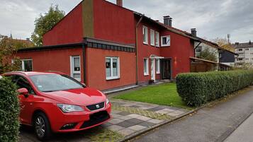 A red two-story house with a paved driveway and a red car parked in front.