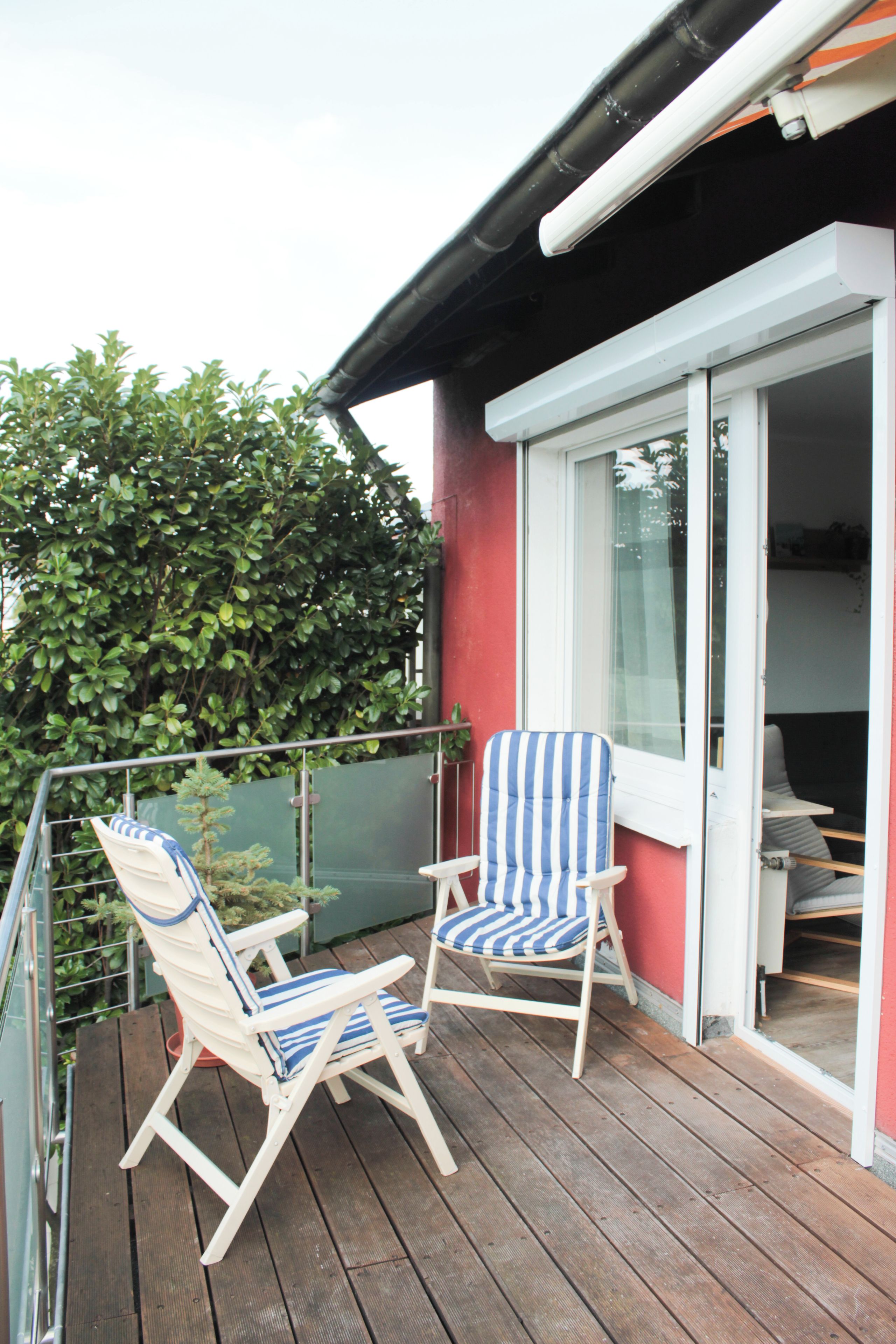 A wooden deck with two striped lounge chairs and a glass door leading to an interior space.