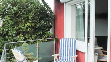 A wooden deck with two striped lounge chairs and a glass door leading to an interior space.