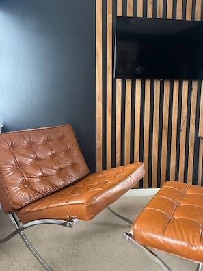 A brown leather chair with a cushioned seat and backrest, positioned in front of a dark wall with vertical wooden slats.