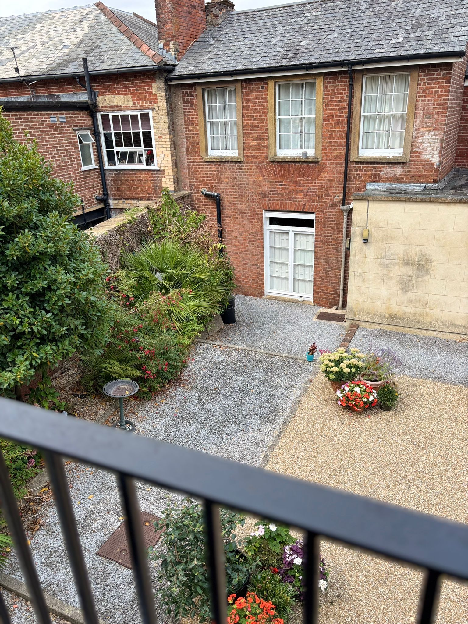 A residential building with a brick facade, a gravel driveway, and a variety of plants and flowers.