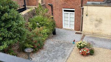 A residential building with a brick facade, a gravel driveway, and a variety of plants and flowers.