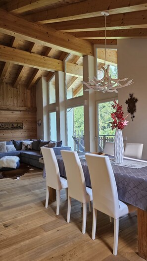 Un espace repas doté d’un plafond en bois, d’une table entourée de chaises blanches et offrant une vue sur l’extérieur.