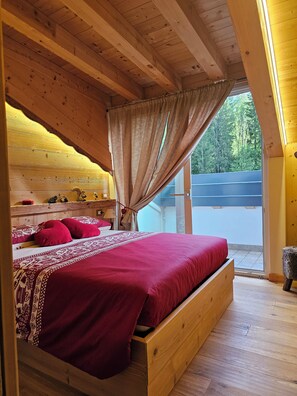 A wooden cabin bedroom with a bed, curtains, and a view of the outdoors. - New Listing (Veneto)