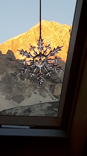 Un flocon de neige décoratif suspendu à une fenêtre, avec vue sur une montagne.
