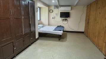 A room with a bed, wardrobe, wall-mounted TV, and an air conditioning unit.