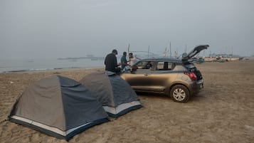A beach with tents and a car with its trunk open.