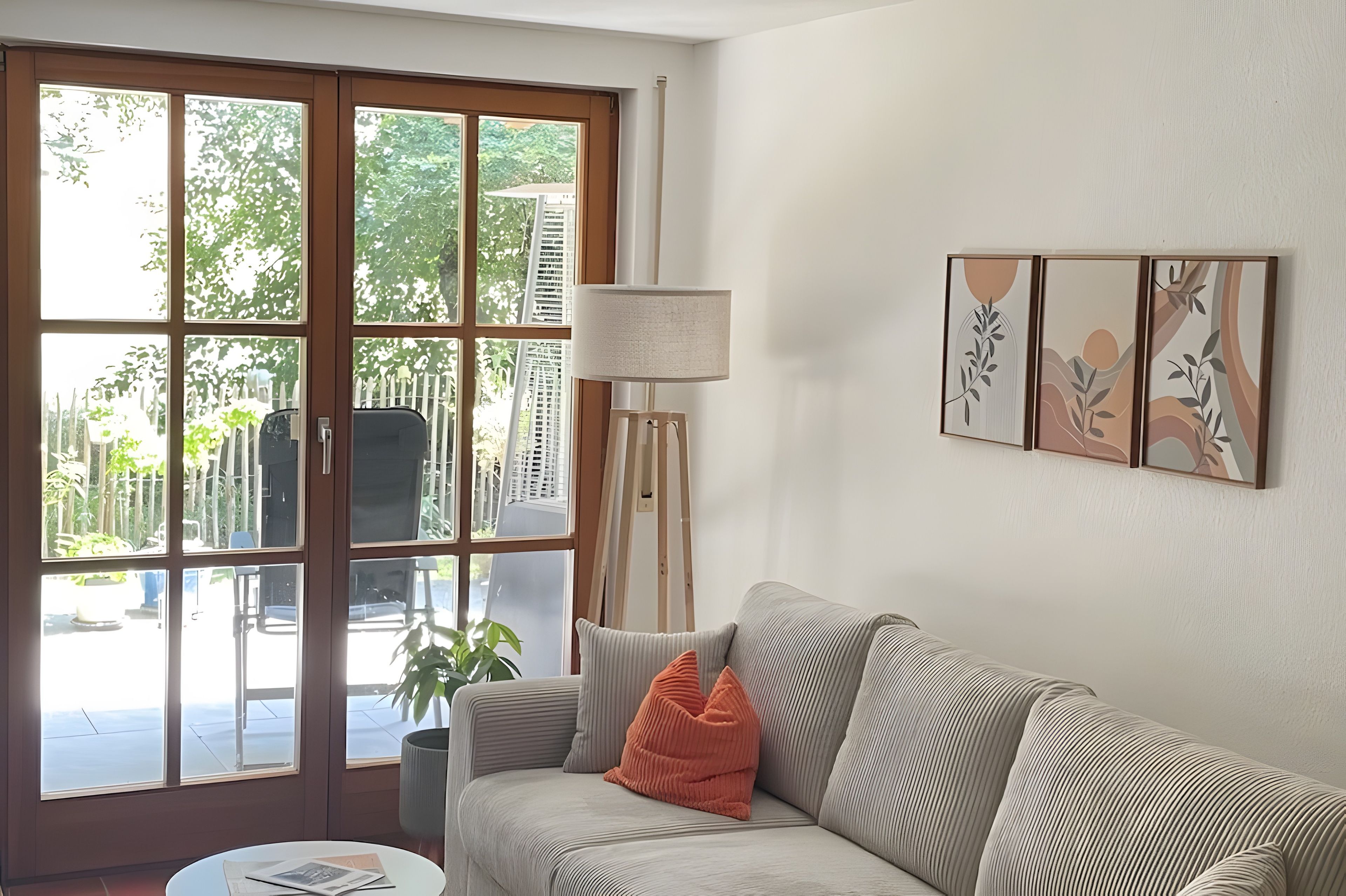 Un salon avec un canapé, une lampe et une vue sur un balcon agrémenté de plantes et d’une clôture.